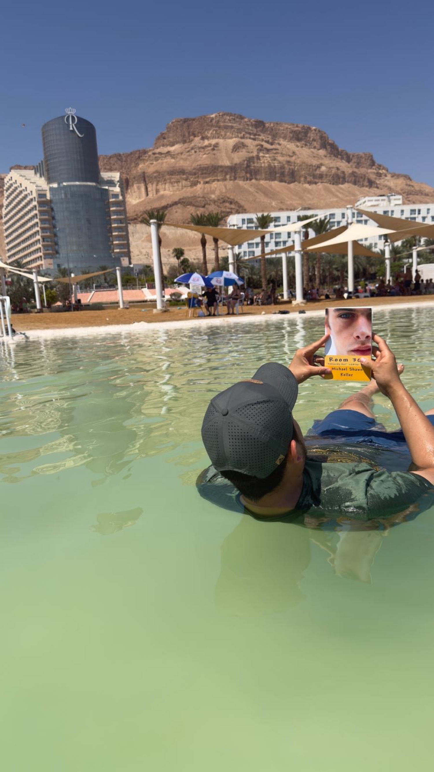 A reader floating in the Dead Sea holding a signed paperback of Room 308